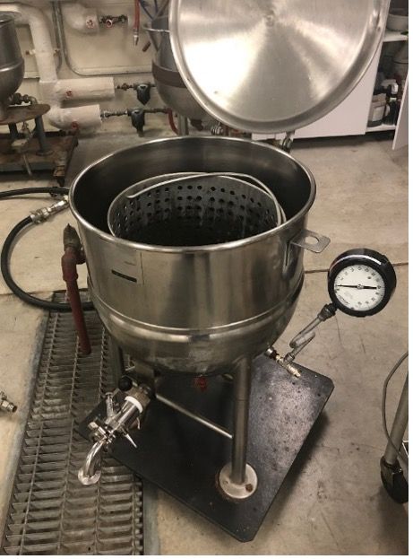 Boil-blanching steam kettle unit with a perforated basket inside used for transferring peaches to and from the kettle.