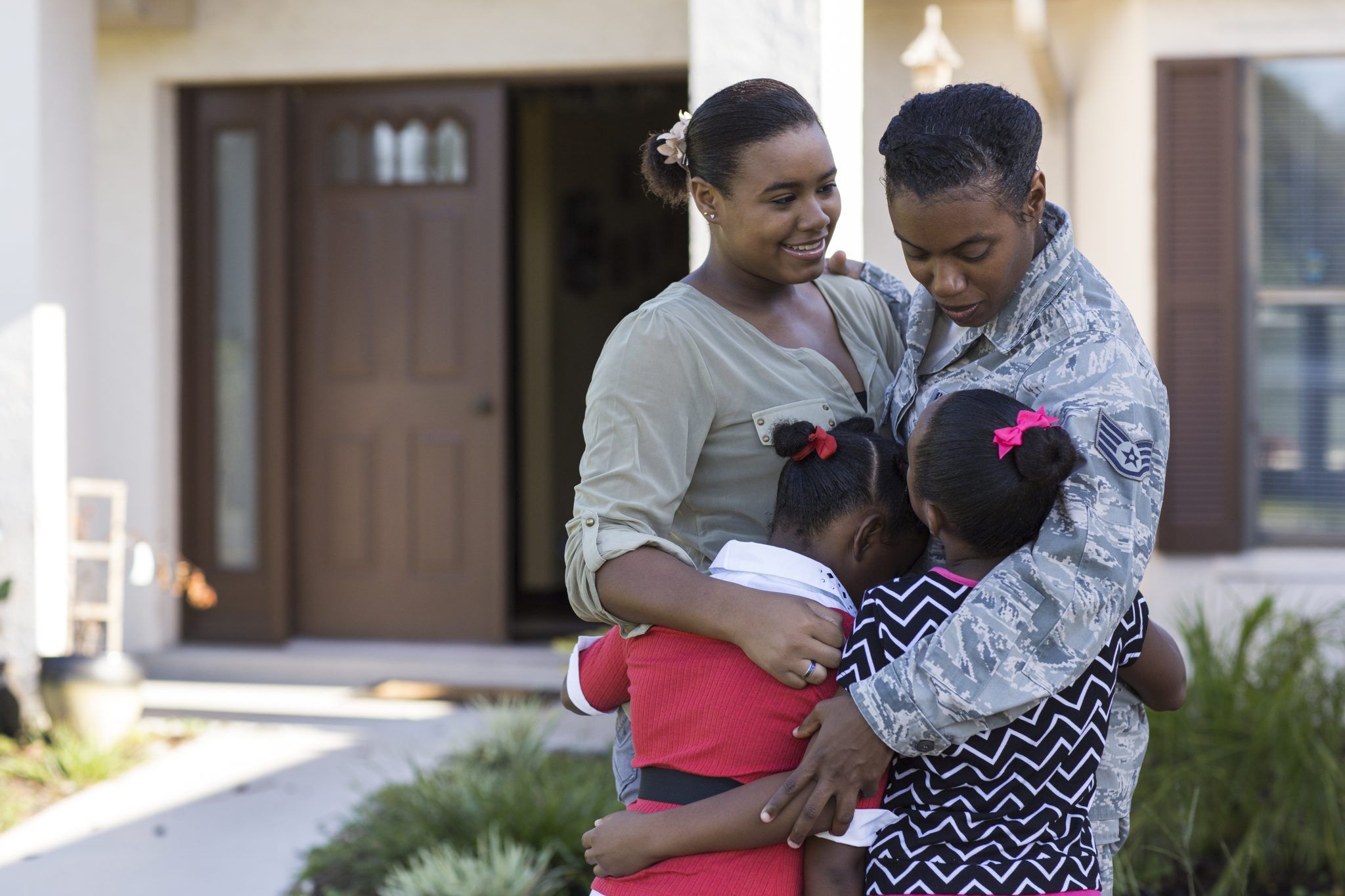 Active duty military mother hugs her three daughters in front of their home. Image used in the 2015 UF/IFAS Extension Calendar. 