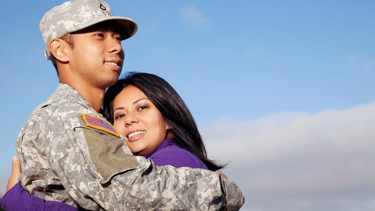 Smiling U.S. soldier and spouse embrace each other in a hug. 