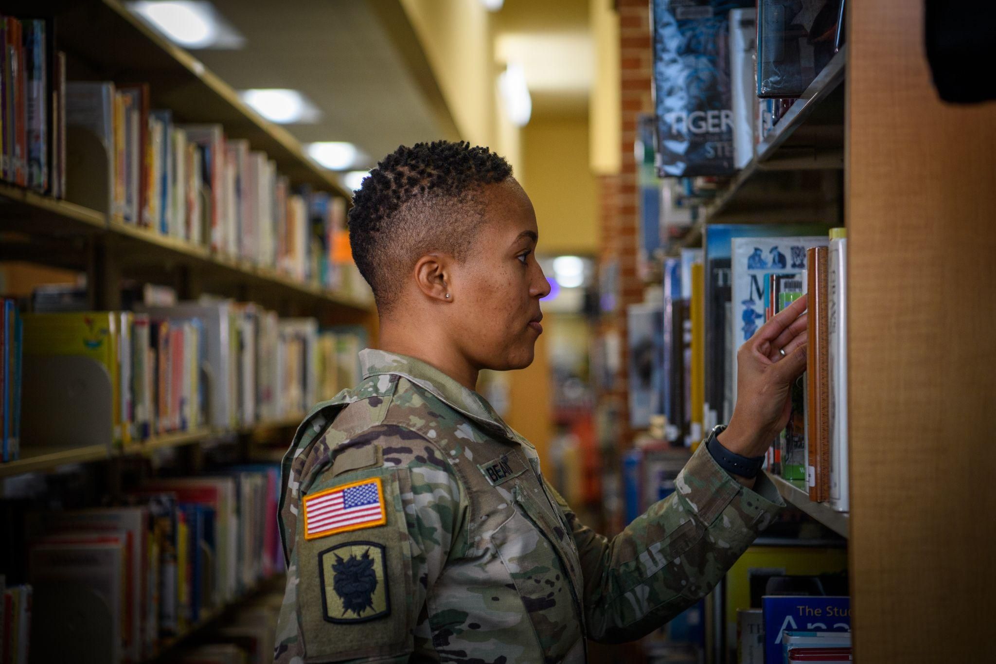 Uniformed service member selects a book from a shelf at the library. 